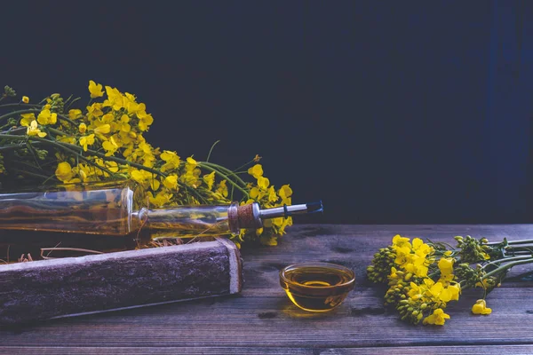 bottle of rapeseed oil near rapeseed flowers on a wooden table on a blue background