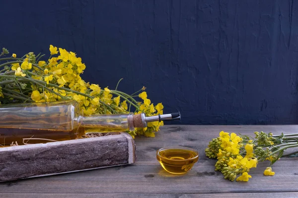 rapeseed flowers near a bottle of rapeseed oil on a wooden table on a blue background