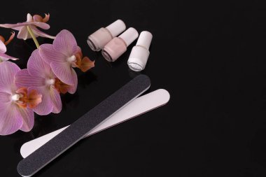 Cam bir masada siyah bir arkaplanda oje, orkide ve tırnak törpüleri bulunur.