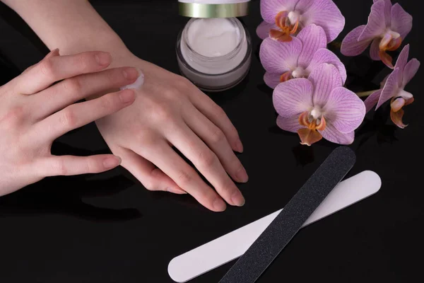 Frauenhände Tragen Handcreme Auf Neben Einer Rosa Orchidee Auf Schwarzem — Stockfoto