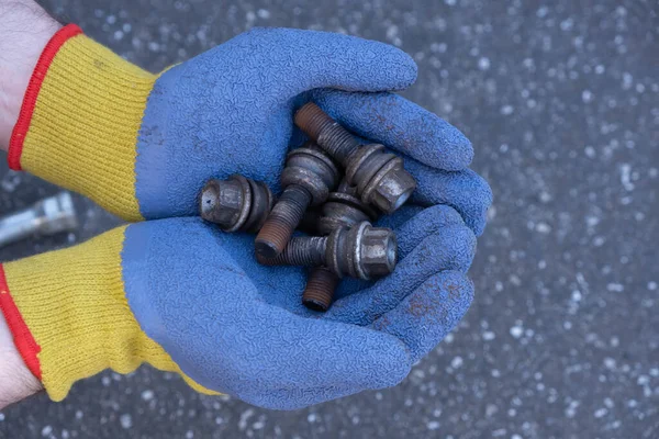 male hands in gloves hold bolts from a car wheel on the street