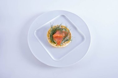 Bir tabakta salatalık, somon ve dereotu uzanır. Beyaz bir arka planda mısır gözlemesinin üzerinde.