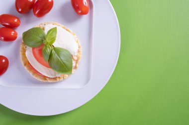 Beyaz bir tabakta mısır ekmeği, üzerinde mozzarella, domates ve fesleğen bulunur.