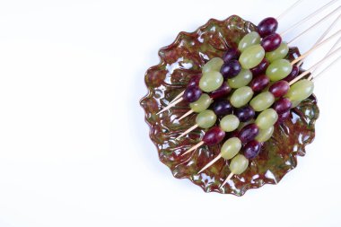 Üzüm ve peynir şişlere konur ve beyaz arka planda bir tabağa konur.