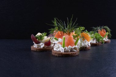 Somon, karides, dereotu ve sos sandviçleri siyah arka planda bir masanın üzerinde yatar.