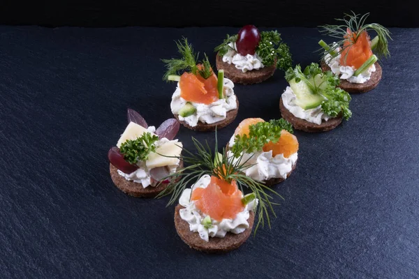sandwiches of salmon, shrimp, dill and sauce on the table on a black background