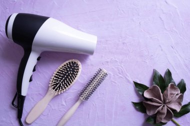 bir saç kurutma makinesi ve tarak, yeşil bir yaprak ve dekorasyonun yanında, dokusal bir arka planda yatar.