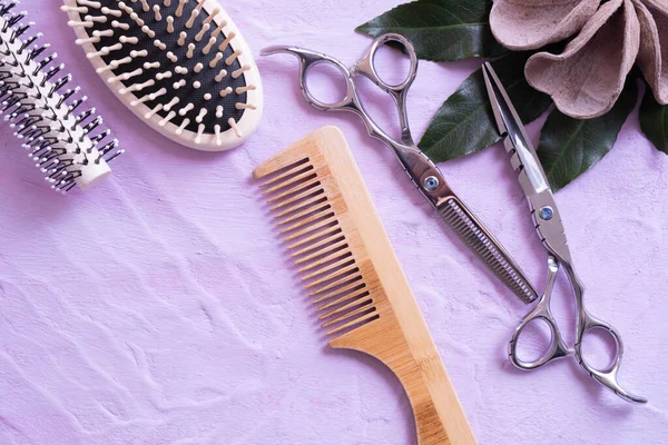 a wooden hair comb, scissors, combs and wood decorations lie on a textural background and everything on a pink background
