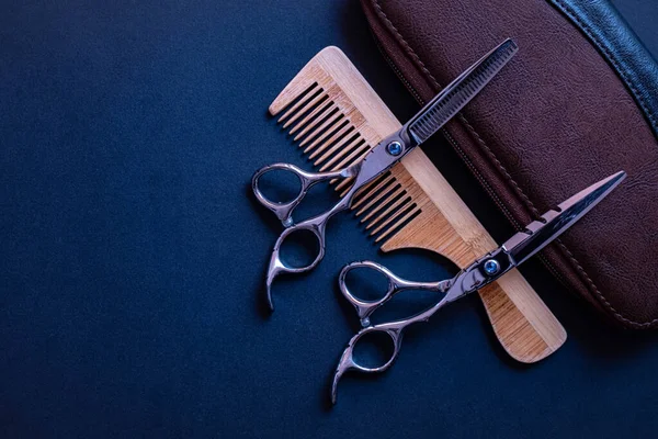scissors for a hairdresser, a bag for them, a wooden comb and wooden decoration lie on a textured background and everything on a blue background