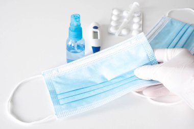 Doktorun elinde bir termometre var. Tıbbi maske, antiseptik ve beyaz bir arka planda, masanın üzerinde haplar.