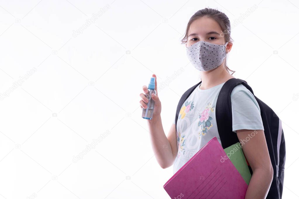 schoolgirl with a gray mask on her face holds an antiseptic and notebook in her hand on a white background