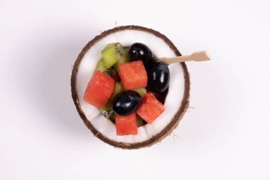 Masadaki beyaz tabakta hindistan cevizli karpuz üzümü ve kivi dilimleri.