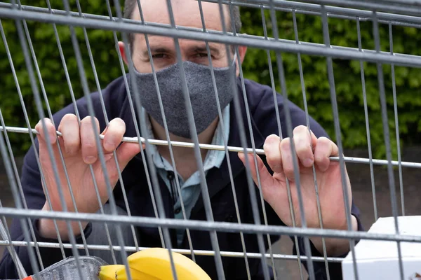 masked man hiding behind bars of shopping carts on the street