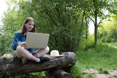İlkbaharda şehir dışında eski bir kütüğün üzerinde dizüstü bilgisayarla oturuyor.