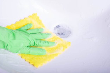 Elinde bez parçasıyla banyodaki lavaboyu beyaz arka planda temizliyor.