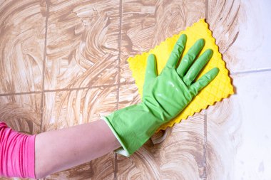 Eldivenli temizlikçi kadın banyoyu temizliyor ve kirli bir duvarı beyaz arka planda yıkıyor.