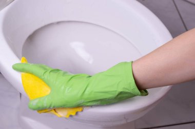 Banyodaki temizlikçi kadın beyaz arka planda yeşil eldivenlerle tuvaleti yıkıyor.