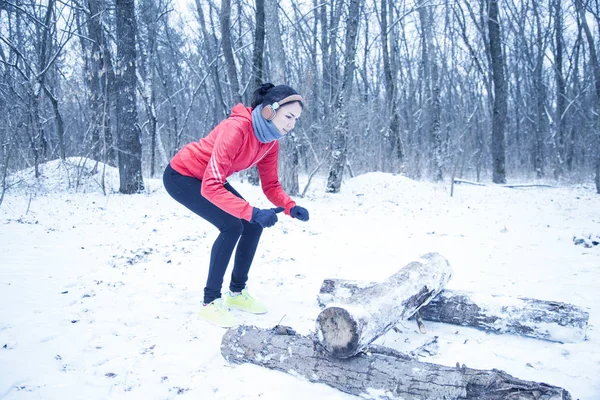 Female runner jogging in cold winter forest wearing warm sporty