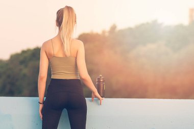 Güzel poposu olan genç bir kadın göle bakıyor. Antrenmandan sonra dinleniyorum.