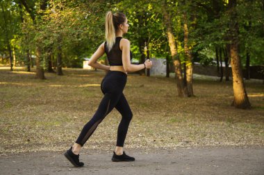 Genç bir kadın parkta koşuyor.