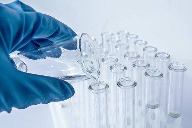 Mavi eldivenli bir el. Sıvıyı şişelerden test tüpüne dök.