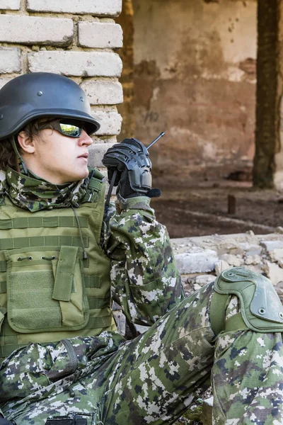 Солдат розмовляє по радіо, сидячи в зруйнованій будівлі. Військові конфлікти та комунікації — стокове фото