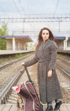 Tren istasyonunda bir çanta ile kız. Tren bekliyor