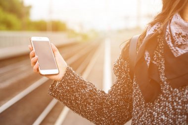 Smartphone bir demiryolu hafif bir arka plan üzerinde bir kadın elinde. Günbatımı