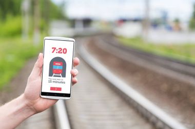 Demiryolu arka plan üzerinde elinde telefon. Smartphone ekranında, treni varış hakkında bilgi. Tren zamanlama