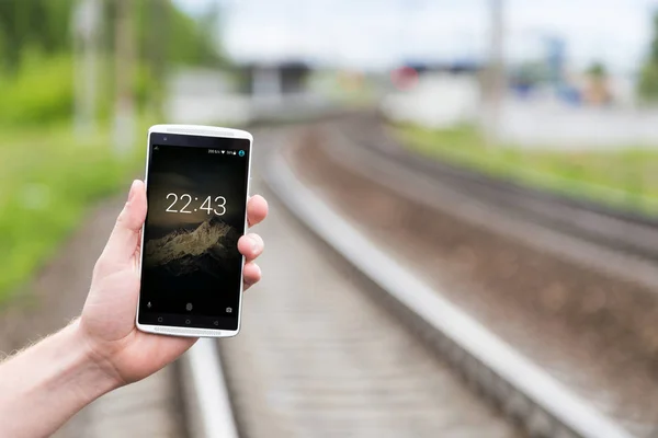 Teléfono en mano en el fondo del ferrocarril. Protector de pantalla en su teléfono con un reloj — Foto de Stock
