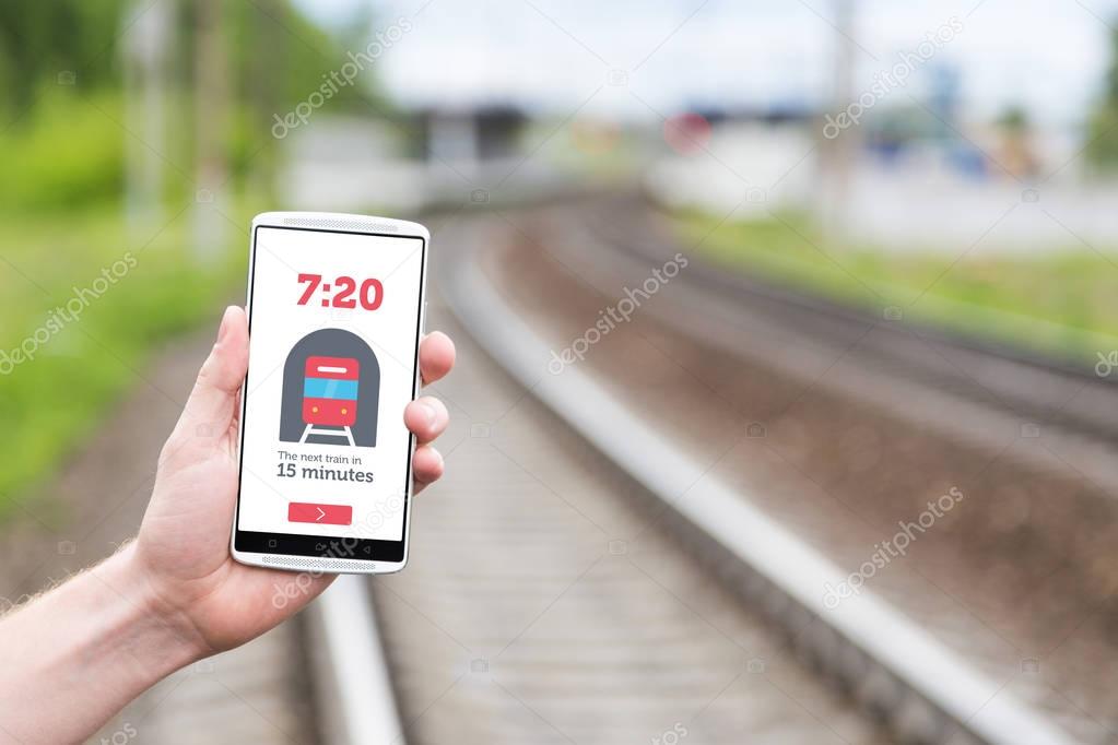 Phone in hand on the background of the railway. On the smartphone screen, information about the arrival of the train. Train schedule
