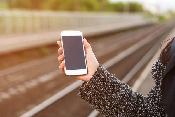 Smartphone en una mano femenina sobre un fondo claro de un ferrocarril . — Foto de Stock