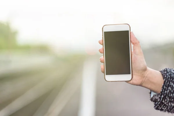 Smartphone en una mano femenina sobre un fondo claro de un ferrocarril . — Foto de Stock