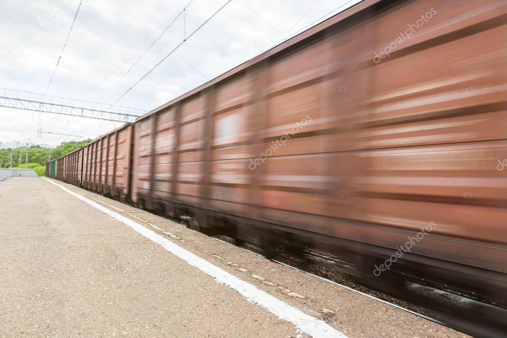 The freight train in motion is passing by the station. Russian Railways