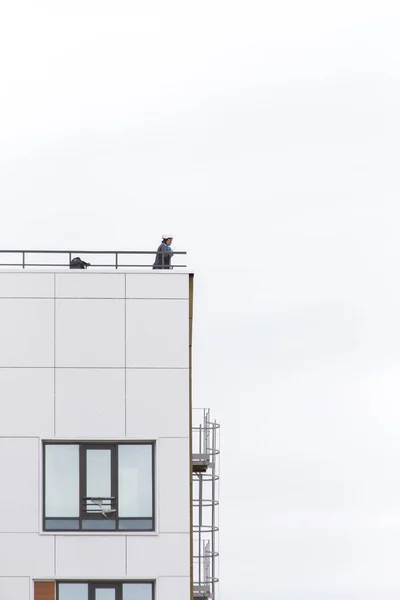 UFA, RÚSSIA - 21 de maio de 2016: Idel Tower. Engenheiro em um capacete fica na borda do telhado de um edifício moderno — Fotografia de Stock