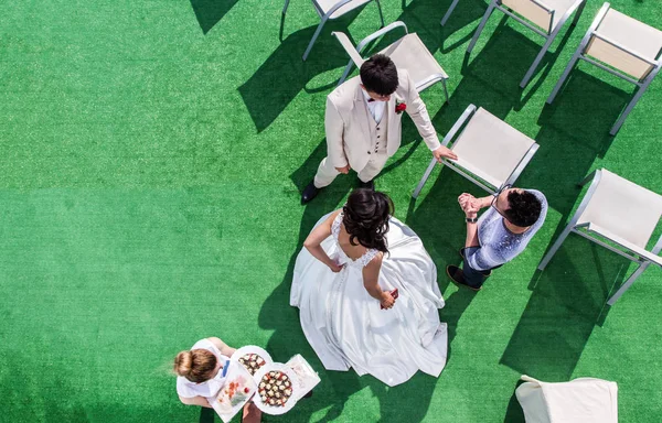 La vista dall'alto dello sposo e della sposa che parlano con l'organizzatore sullo sfondo di sedie bianche e erba verde e i camerieri che distribuiscono cibo . — Foto Stock