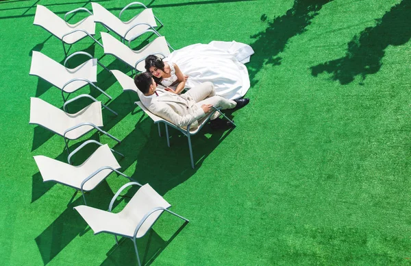 La novia y el novio están sentados en sillas blancas sobre un fondo de hierba verde solo antes del comienzo de la ceremonia . —  Fotos de Stock