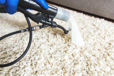 Temizlik servisi. Eldivenli hademe ve elektrikli süpürgeli beyaz halıyı profesyonel ekipmanlarla temizliyor.
