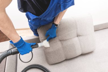 Temizlik servisi. Eldivenli ve elektrikli süpürgeli adam. Profesyonel ekipmanlı temiz kanepe.