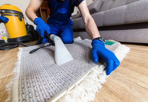 Serviço de limpeza. Homem zelador em luvas e vácuo uniforme limpo tapete branco com equipamento profissional — Fotografia de Stock