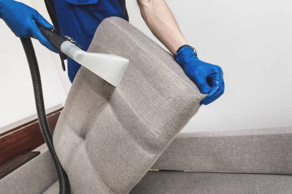 Serviço de limpeza. Homem zelador em luvas e sofá limpo vácuo uniforme com equipamento profissional — Fotografia de Stock