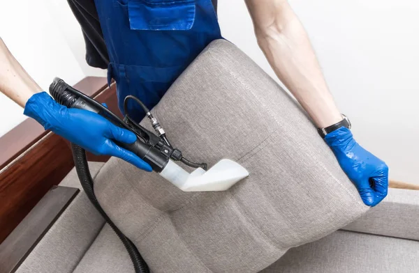 Serviço de limpeza. Homem zelador em luvas e sofá limpo vácuo uniforme com equipamento profissional — Fotografia de Stock