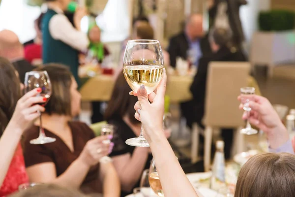 people at the table at a solemn event clink glasses and celebrate. raised hands with glasses