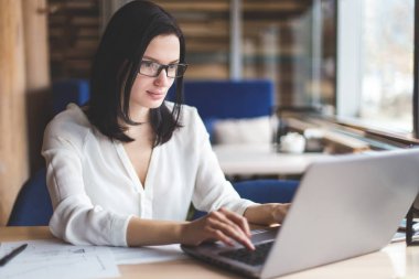 Esmer iş kadını gözlüklü dizüstü çalışma ve rahat kafe atmosfer penceresinde yakınındaki belgeleriyle