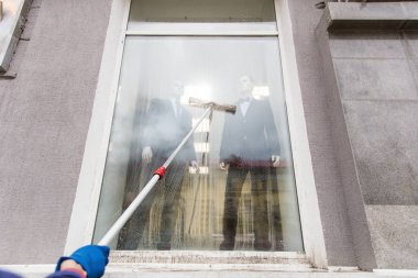 Mavi tulum genç erkek temizlikçi binanın cephe, windows ve mağaza açık yıkar. Temizleme Servisi yakın çekim