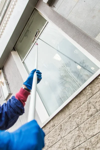 Een jonge mannelijke schoner in blauwe overalls wast gebouw van gevel, ramen en winkel voorkant. Schoonmaak Service close-up — Stockfoto
