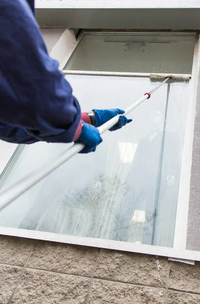 Un giovane uomo più pulito in tuta blu lava la facciata dell'edificio, le finestre e la parte anteriore del negozio. Impresa di Pulizia close up — Foto Stock