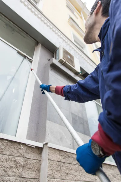 一个年轻的男性清洁工在蓝色工作服洗涤窗口和商店前面。清洁服务 — 图库照片