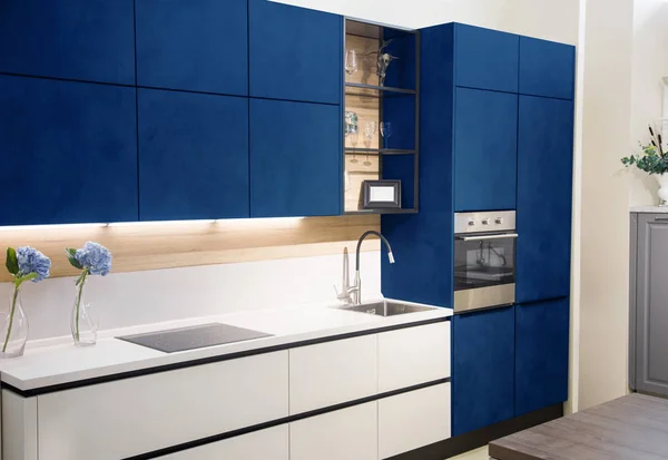 Modern blue kitchen interior with white brick walls, wooden countertops with a built in sink and a cooker.