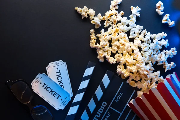Billete, palomitas de maíz, tira de película y aplausos, películas y concepto de entretenimiento sobre fondo negro con luz de neón azul, flatlay —  Fotos de Stock